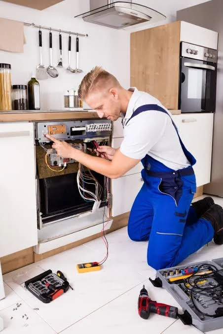 Technician testing exposed dishwasher electronics beside an open tool kit