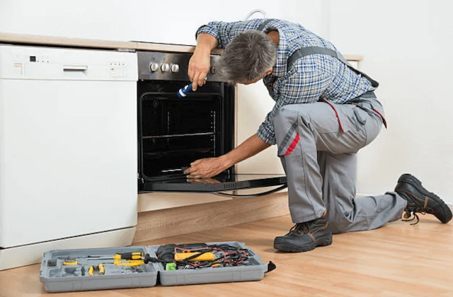Technician examining an open oven with a flashlight and nearby tools
