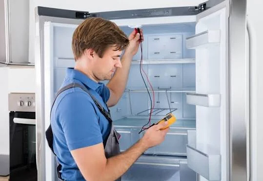Technician using a multimeter inside an open refrigerator
